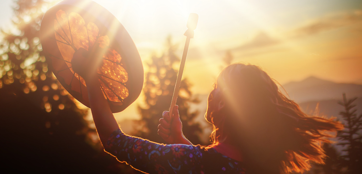 A woman plays a drum. The sun shines on her face.